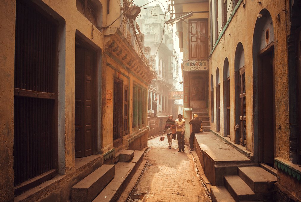A narrow lane in old Varanasi with colourful shops, temple entrances, and locals going about their day